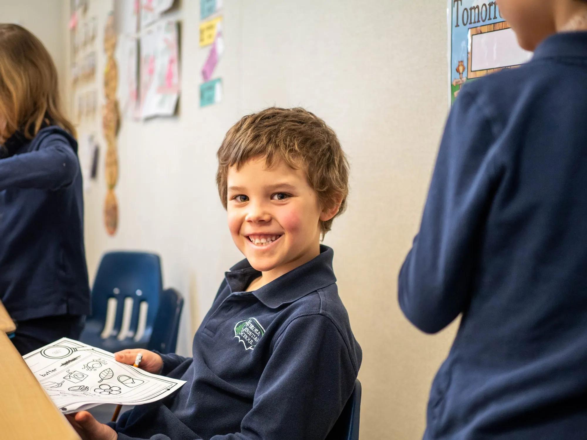 A smiling elementary student in a navy school polo working at his desk